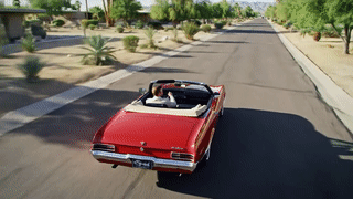 Un uomo alla guida di un&#39;auto cabriolet rossa a Palm Springs, in stile anni &#39;70.